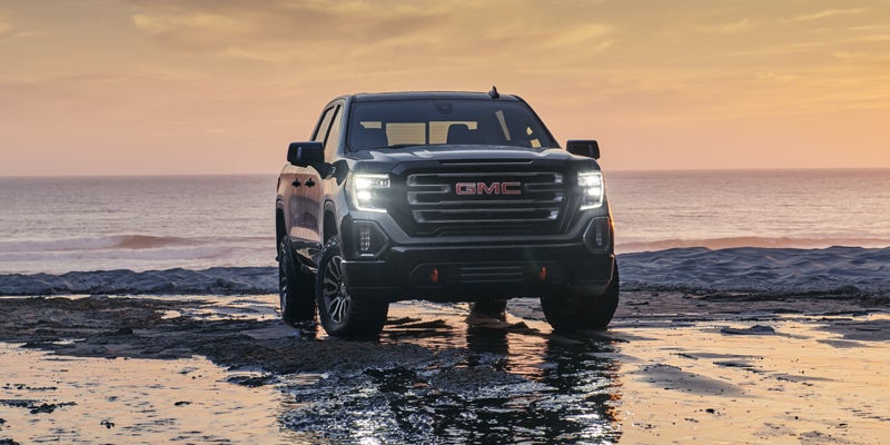 A GMC Sierra 1500 in front of a lake, with water beneath it and mirroring the vehicle.