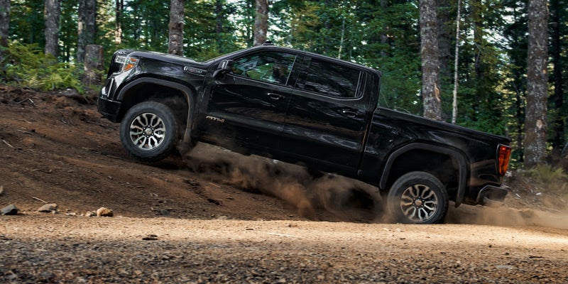 GMC Sierra 1500 driving on a dusty road, with trees in the background.