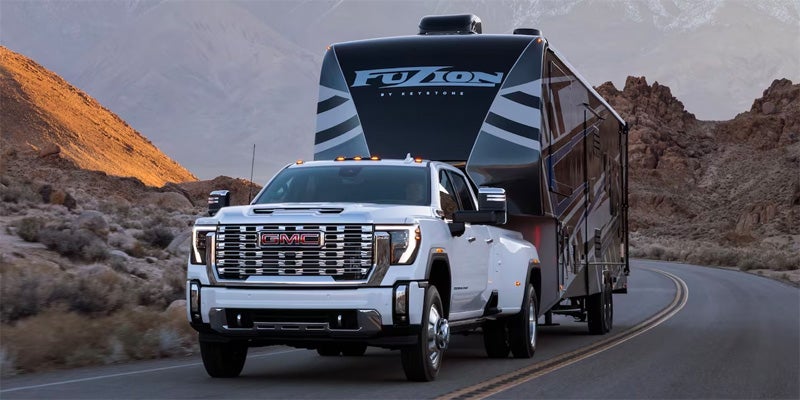 A white GMC Sierra HD pickup truck towing a large black trailer